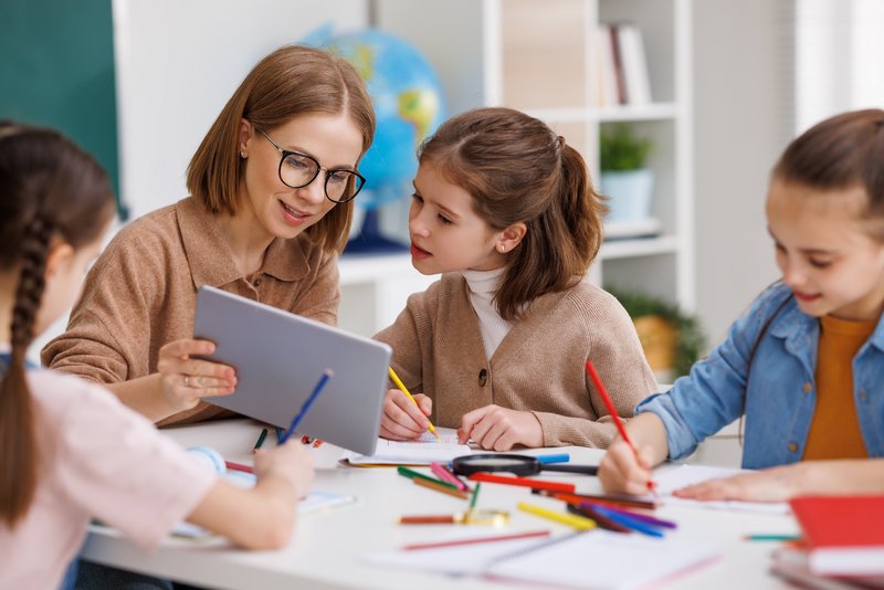 Junge Grundschullehrerin mit Schülerin am Tablet