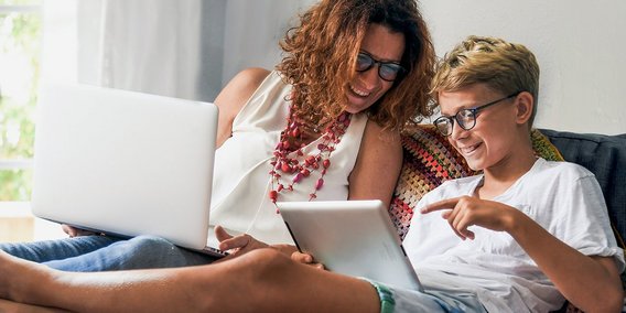 Mutter und Sohn mir Rechner und iPad auf dem Sofa