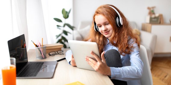 Mädchen mit Tablet und Kopfhörern am Schreibtisch