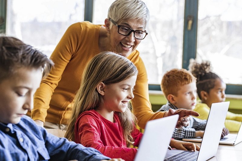 Ältere Lehrerin mit Grundschülern an Laptops